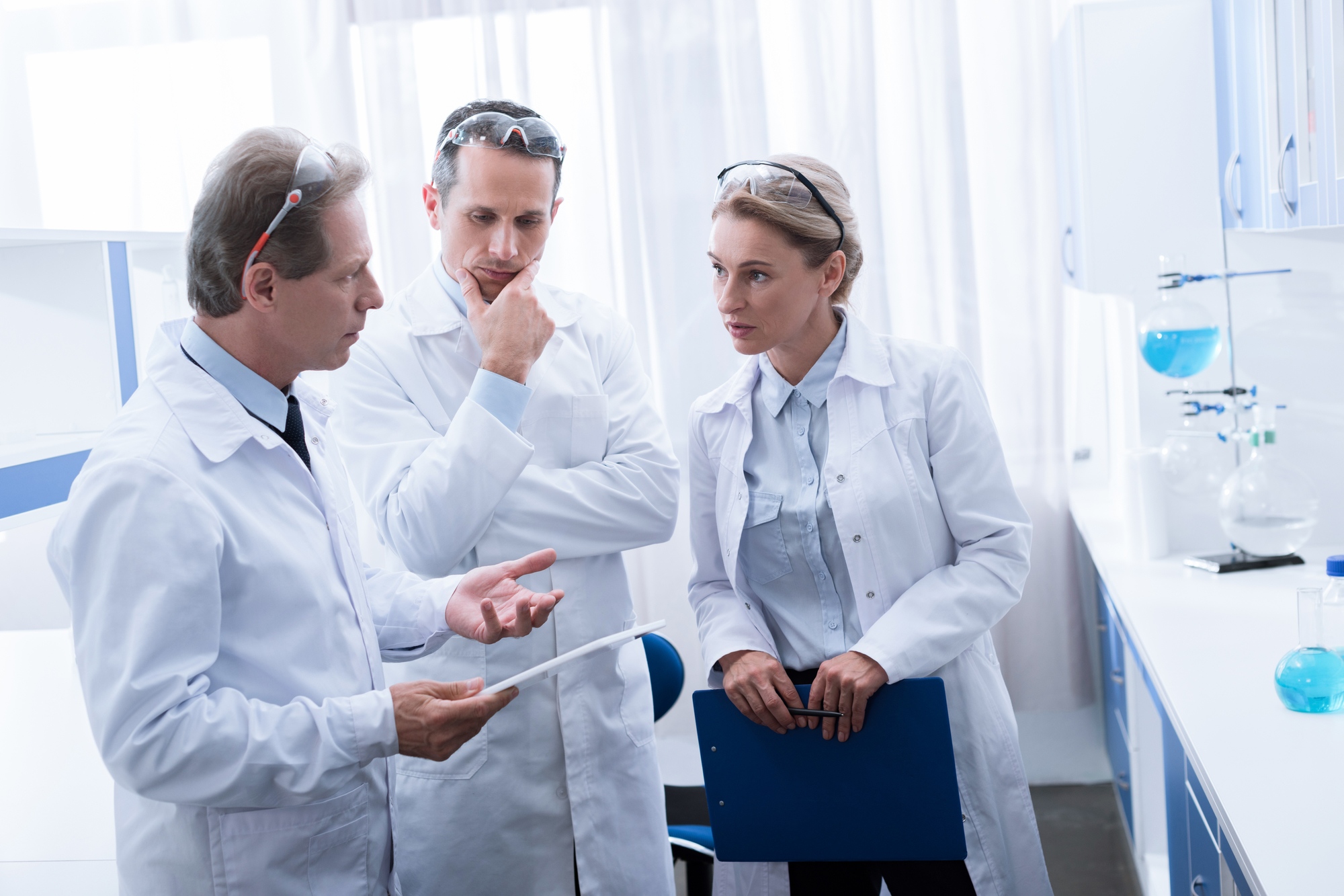 Concentrated colleagues in white coats standing and talking in chemical lab