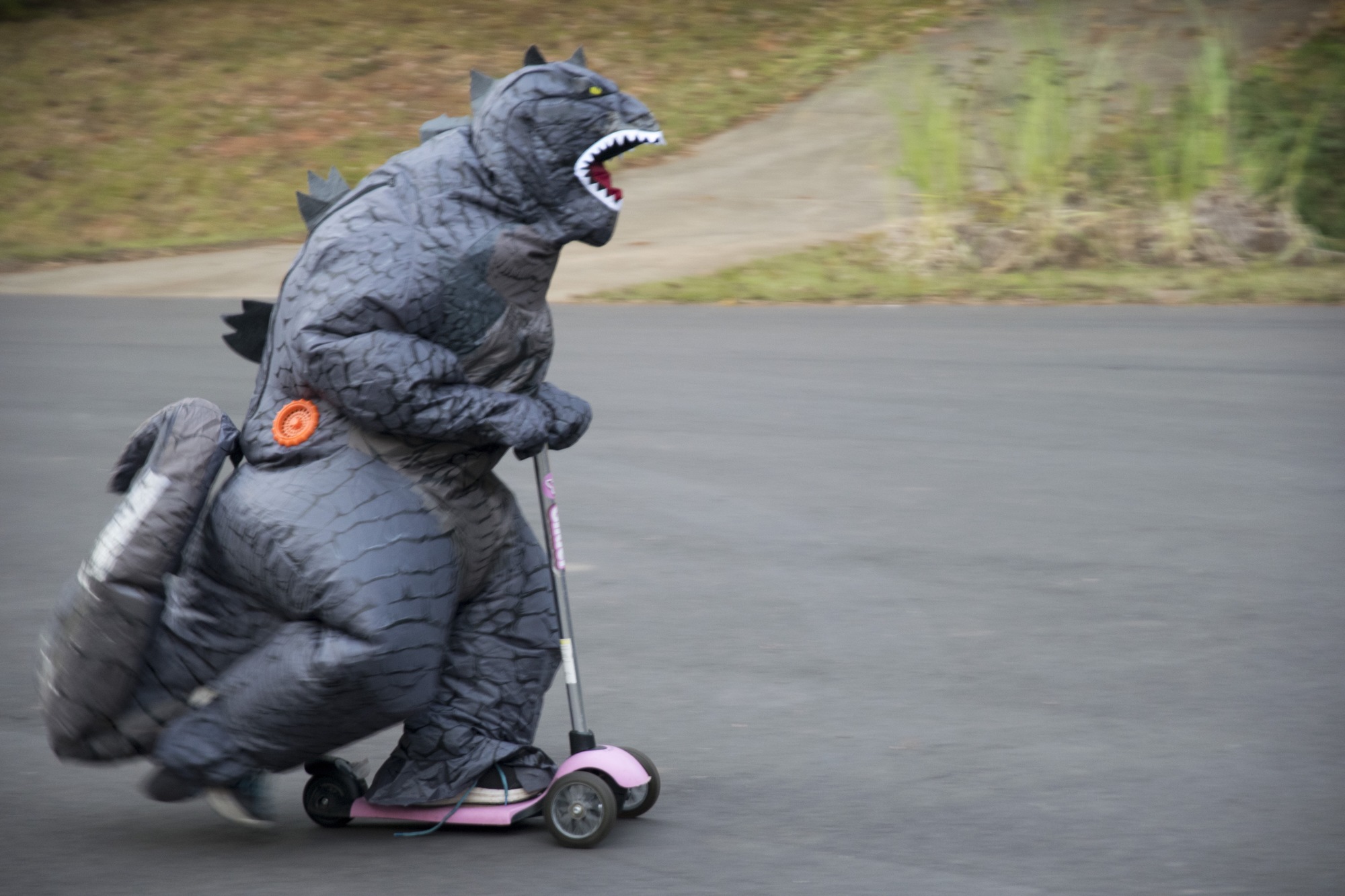 child in an inflatable godzilla costume on a scooter