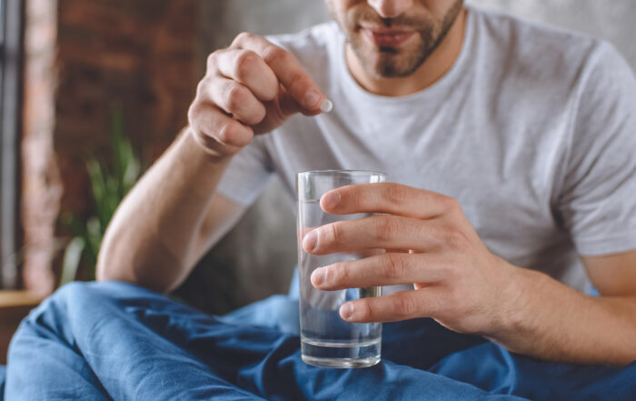 cropped image of young man with hangover putting pill in glass of water in bed at home