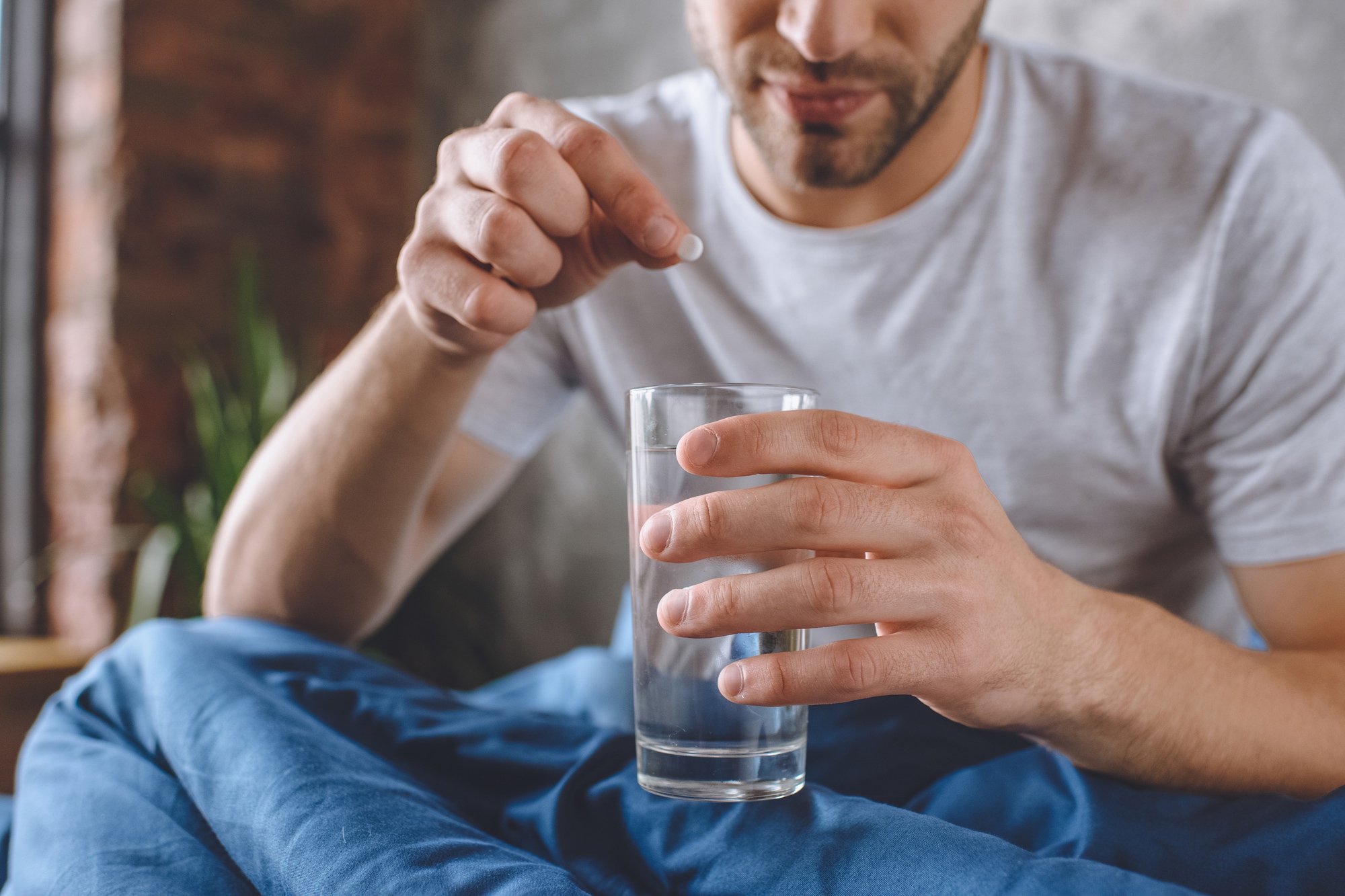 cropped image of young man with hangover putting pill in glass of water in bed at home